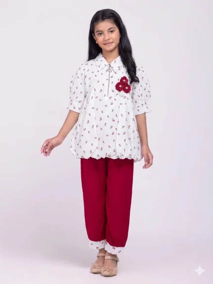 Product Description: Top: A white cotton blouse with a classic collar, short puff sleeves, and an all-over small cherry or floral print. It is accented with a decorative red floral brooch. Pants: Matching maroon or deep red trousers with a relaxed fit. These often feature cuffed hems that repeat the print from the top for a coordinated look. Material: Generally made from soft, breathable 100% soft fabric, suitable for summer and warm weather.